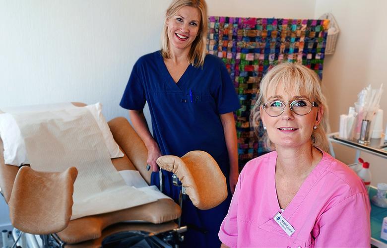 Bildtext: Foto på en leende sköterska och en gynekolog bredvid en gynekologstol. 